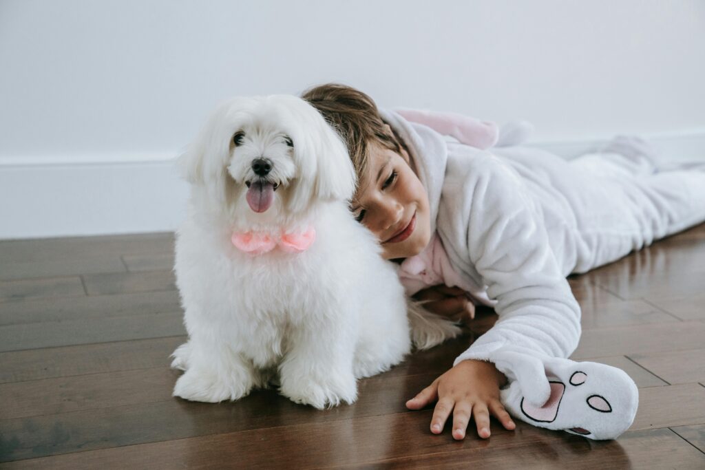 A smiling child in a bunny costume cuddling with a Maltese dog indoors.